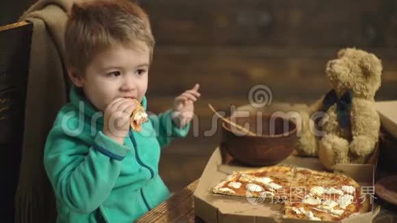 一个男孩在木制背景下吃披萨。 小男孩把一片披萨隔离在木头上