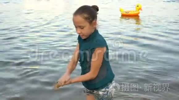 日落时分，一个小女孩在海滩上玩耍，在平静的水背景下建造了一座沙塔。 肖像。 关闭