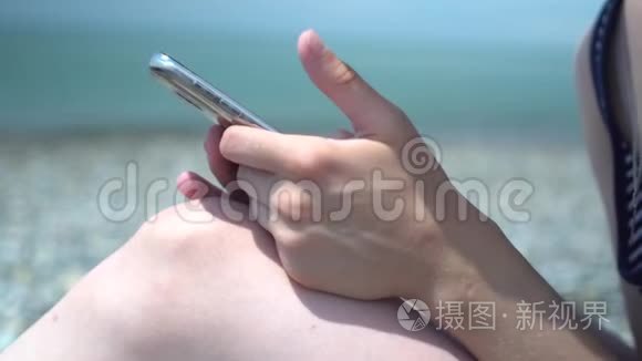 在海岸模糊背景下，年轻女性用智能手机特写。 休息和技术。 上网冲浪