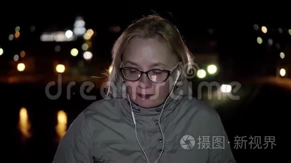 女孩戴着眼镜和耳机站在夜间长廊上，哼着什么，跳舞摇头。