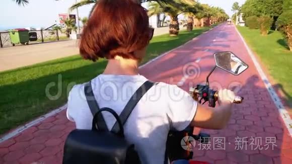 在度假小镇的红自行车道上，女人骑着电动自行车骑着棕榈树