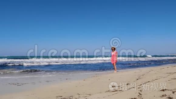 年轻快乐的女人走在海滩上，戴着红色的裙子和太阳镜把帽子扔掉。 强烈的风浪和蓝色的天空
