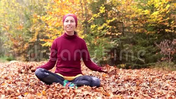 一个年轻的女孩坐在森林的空地上，兴高采烈地抛出黄色的叶子。