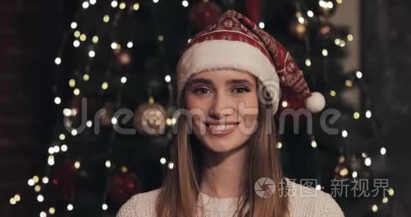 美丽的白种人年轻女性戴着圣诞帽站在舒适的圣诞节圣诞树附近的画像