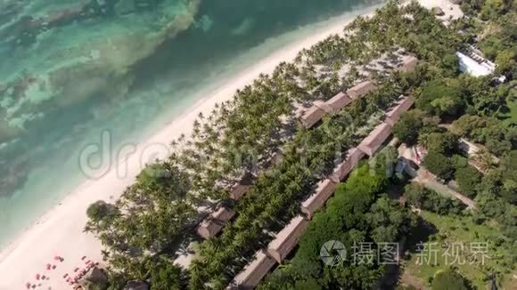 在沙滩上的海浪、绿棕榈树、酒店、房屋和度假胜地的无人机拍摄。