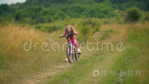 女孩骑自行车在长满青草的马路上