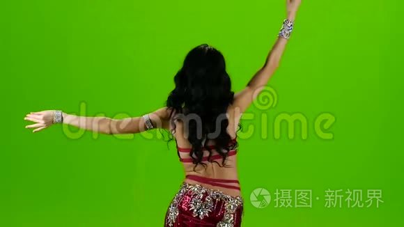 女人站在服装后面，带着装饰品跳舞肚皮舞。 绿色屏幕。 慢动作