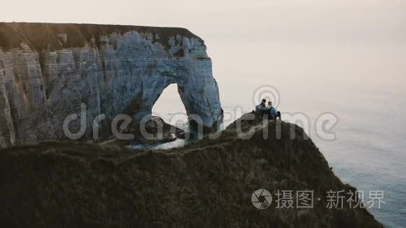 美丽的后景，快乐的男人和女人坐在一起，观看诺曼底海岸悬崖顶部的日落海洋。