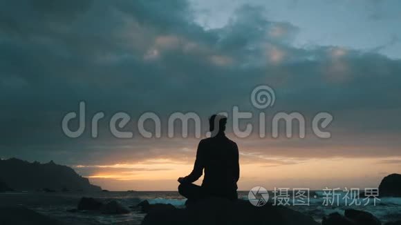 一位妇女坐在岩石上的剪影，日落时，在加那利群岛特内里费的贝尼霍海滩观察海浪。