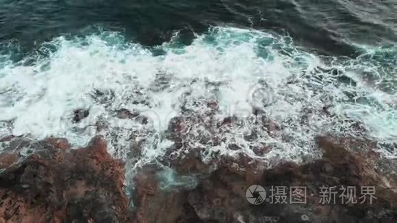 惊涛骇浪在岩石上撞击和扩散的无人机顶景图。 白色和蓝色的海浪飞溅