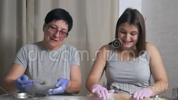 一个怀孕的女孩和她的母亲坐在家里厨房的一张桌子旁，午餐准备饺子和肉末，卷起来