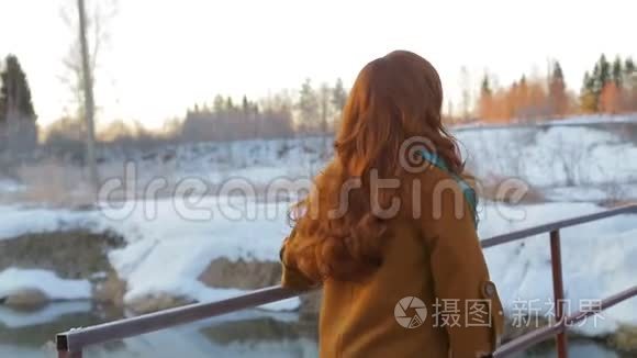 一位年轻的红发女子在日出时沿着桥过一条小河。