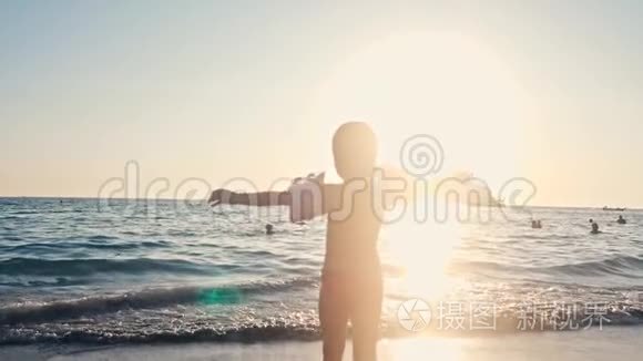 快乐的孩子在美丽的夕阳下跑进大海的剪影。 婴儿在沙滩向水冲去，后方