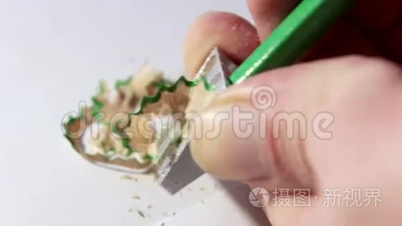 削尖一支简单的绿色铅笔，用一把削刀，男性手放在一个浅色的背景上。