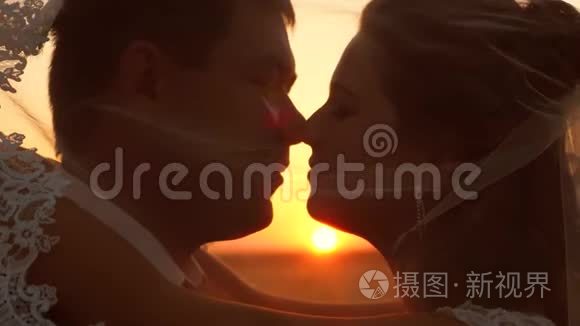 新娘和新郎在日落时亲吻和拥抱。 特写镜头。 浪漫的情侣在日落时接吻。 幸福的概念