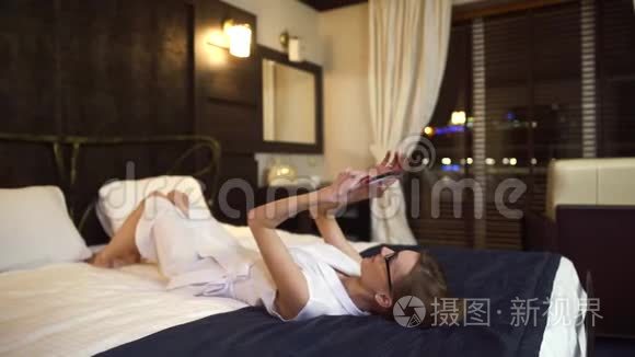 漂亮的女商人戴着眼镜躺在床上，手里拿着平板电脑