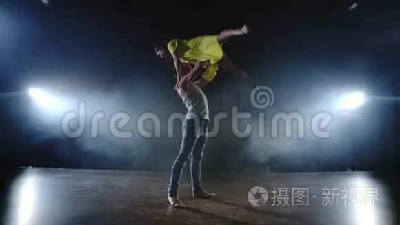 两名现代芭蕾舞演员正在舞台上用烟熏火燎的方式跳舞，一名男子举起他的舞伴，旋转进来