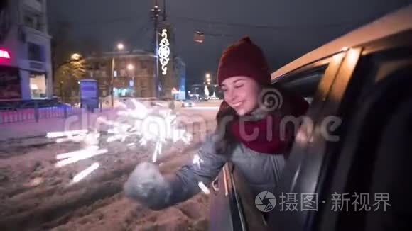 年轻快乐的女人站在车窗外，在下雪的冬夜玩着火花。 漂亮女孩开车很有趣