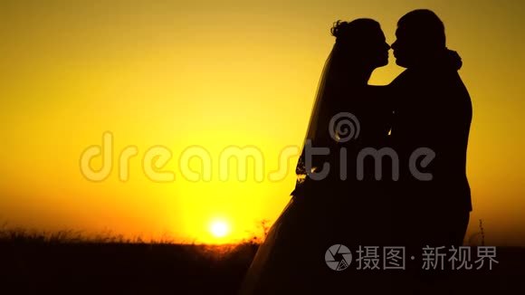 一对情侣在夕阳下相爱的剪影。 年轻的已婚夫妇在日落时亲吻和拥抱。 已婚