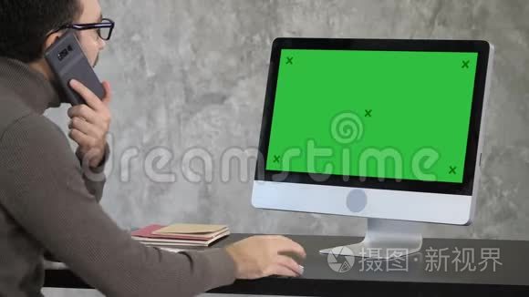 严重集中的男性上班族用手机打电话，在电脑上工作。 绿色屏幕模拟显示。