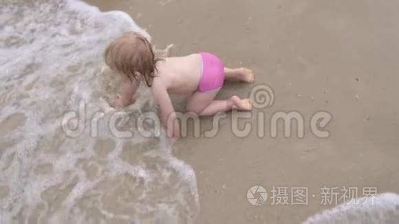 婴儿在波浪中在水面上爬行。 小女孩在沙滩上潮湿的沙滩上爬行..