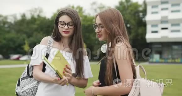 两个十几岁的女孩在校园里一起聊天。 两名女大学生在户外大城市建筑时