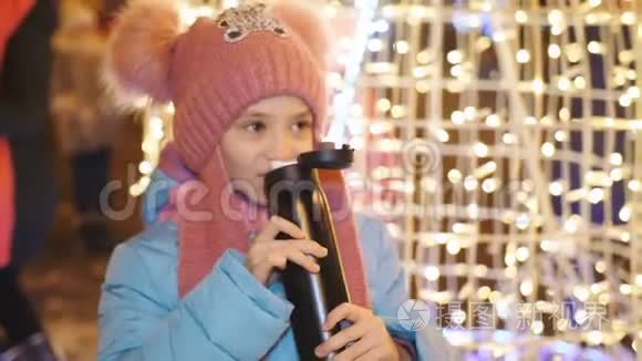 在市中心的圣诞晚会上，小女孩喝着热水瓶里的茶。