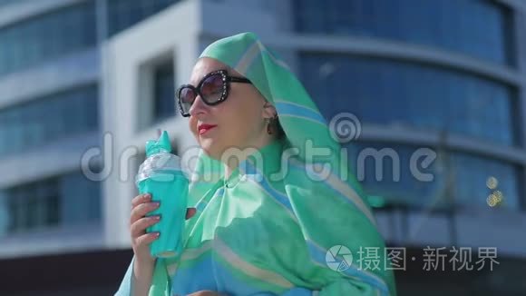 一位年轻的穆斯林妇女，戴着浅色围巾和太阳镜，背景是现代建筑。
