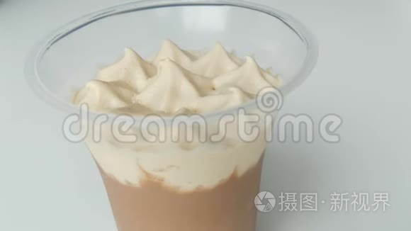 生奶油和巧克力在塑料杯中的甜点。 带茶匙的女性手可以去除奶油的顶部