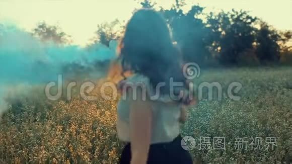 年轻迷人的黑发女孩穿着裙子，带着蓝色的烟雾弹在田野上。 女孩开心地笑着享受
