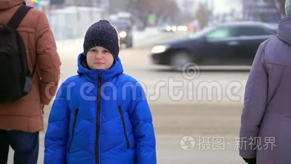 穿着蓝色羽绒服的少年站在街上。 汽车在后台，男孩在看。