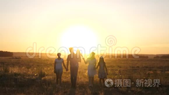 幸福的家庭在夕阳下漫步在田野里。 爸爸妈妈和女儿在阳光下在公园里散步。 儿童和