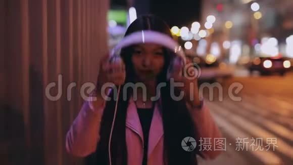 亚洲女人在城市的夜晚戴上耳机走路
