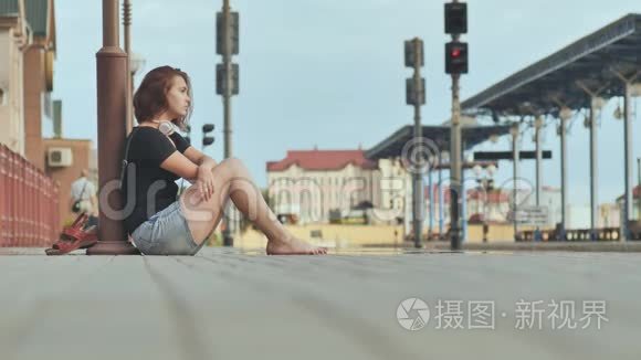 悲伤的女孩坐在火车站的瓷砖上戴着耳机。