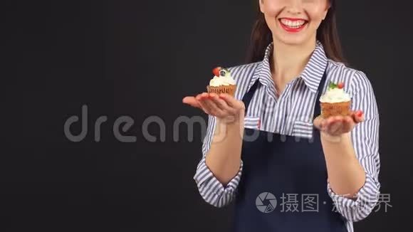 年轻女子手里拿着纸杯蛋糕的糕点师，微笑着对着镜头