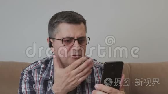 一个中年男人坐在沙发上，用智能手机里的视频通话与另一个人交流。