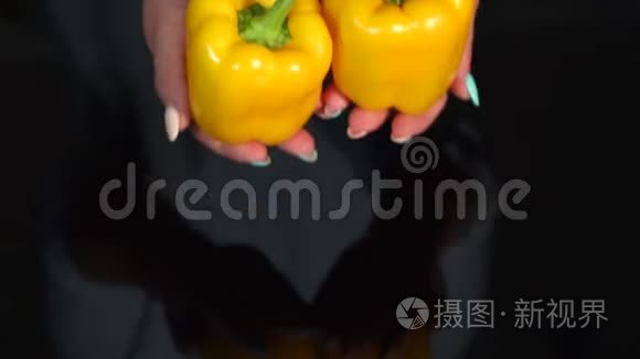 女人的特写，黑色背景上拿着成熟的黄椒。 慢动作。