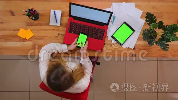 一位年轻的白种人员工用平板电脑用手机在办公桌上用绿色屏幕进行特写拍摄