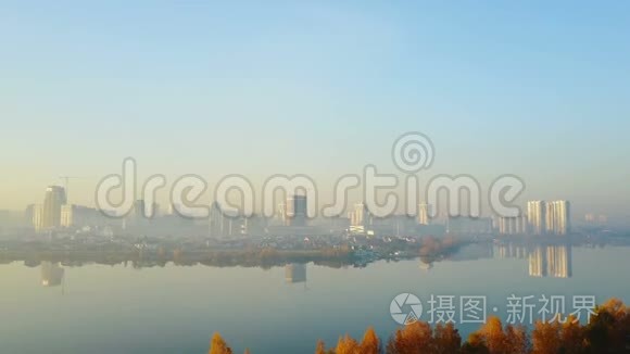 无人机飞向大日出城市天际线风景，高楼之上静湖和黄秋林树..