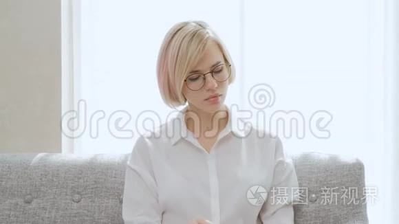 一个年轻漂亮的金发女人戴着眼镜坐在沙发上用手机说话