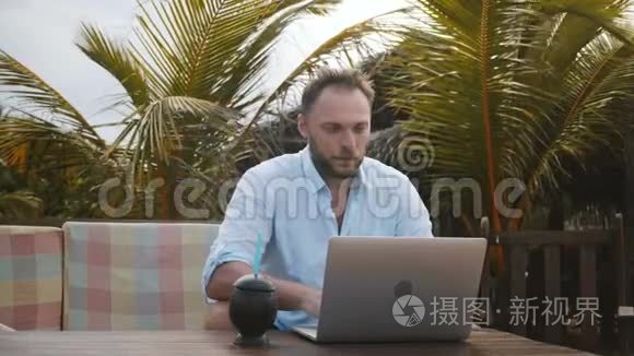 中镜头集中成功的中年商人使用笔记本电脑移动办公室在异国棕榈树海滩度假村。