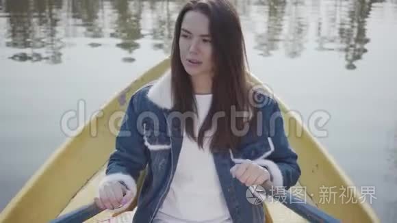 一个迷人的女孩穿着牛仔夹克漂浮在湖面或河流上的船上的肖像。 很漂亮的黑发女人