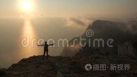 一位年轻女子伸出双臂，从一座高山望着海面上美丽的日落