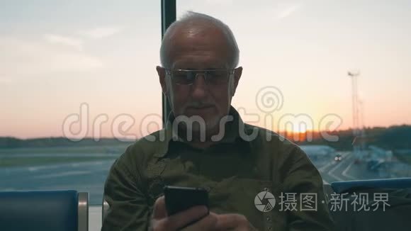 一位白发苍苍、胡须苍白的老人正在机场等候登机，他用智能手机打发时间
