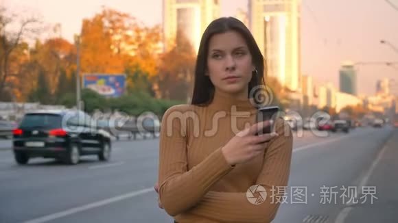 疲惫的黑发白种人女孩紧张地站在路边，手里拿着电话的肖像。