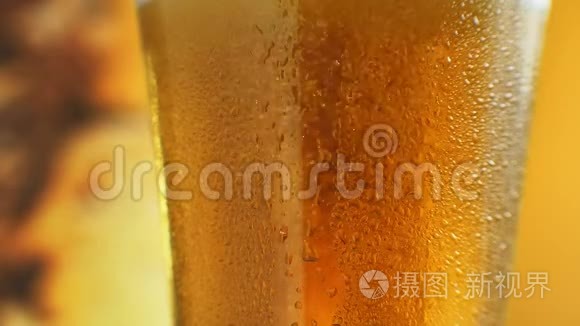 橙色液体玻璃中泡沫的宏观镜头。 在装有水滴的杯子里喝冷光啤酒。 手工艺啤酒