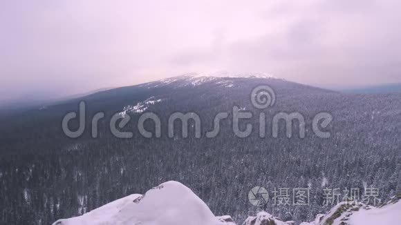 一个背着背包的年轻人，站在一座白雪覆盖的山上，欣赏着风景。