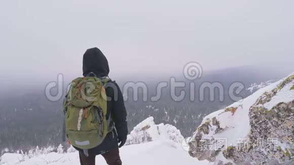 一个背着背包的年轻人，站在一座白雪覆盖的山上，欣赏着风景。