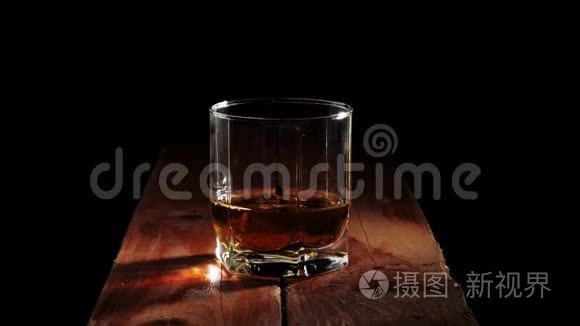 豪华威士忌。 冰块在黑色背景的棕色木桌上，溅到一个带有金色威士忌的玻璃杯中。
