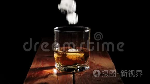 豪华威士忌。 冰块在黑色背景的棕色木桌上，溅到一个带有金色威士忌的玻璃杯中。
